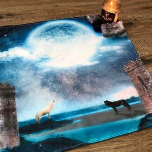 May include: A blue and white tapestry with a full moon, two wolves howling at the moon, and two stone towers. The tapestry has a distressed, vintage look.