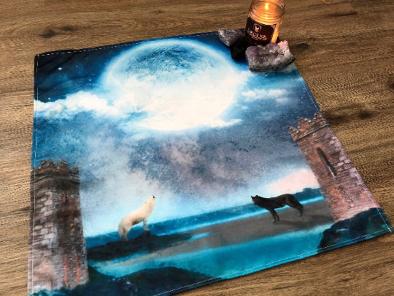 May include: A blue and white tapestry with a full moon, two wolves howling at the moon, and two stone towers. The tapestry has a distressed, vintage look.