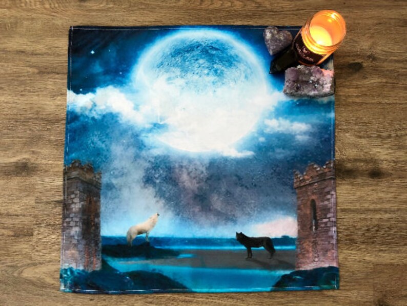 May include: A blue and white tapestry with a full moon, clouds, and two wolves howling at the moon. The tapestry has two stone towers on either side.