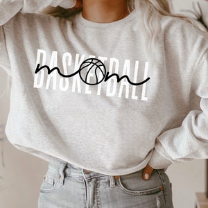 Puede incluir: Una sudadera gris con el texto "Basketball Mom" en letras blancas y un gr&aacute;fico de baloncesto negro.