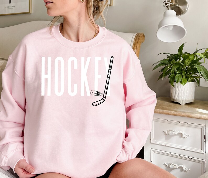 May include: A pink sweatshirt with the word "HOCKEY" printed in white and a black and white illustration of a hockey stick and puck.