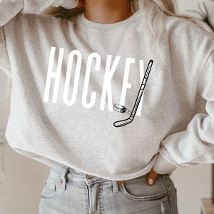 May include: A gray sweatshirt with the word "HOCKEY" and a hockey stick and puck graphic printed on the front.