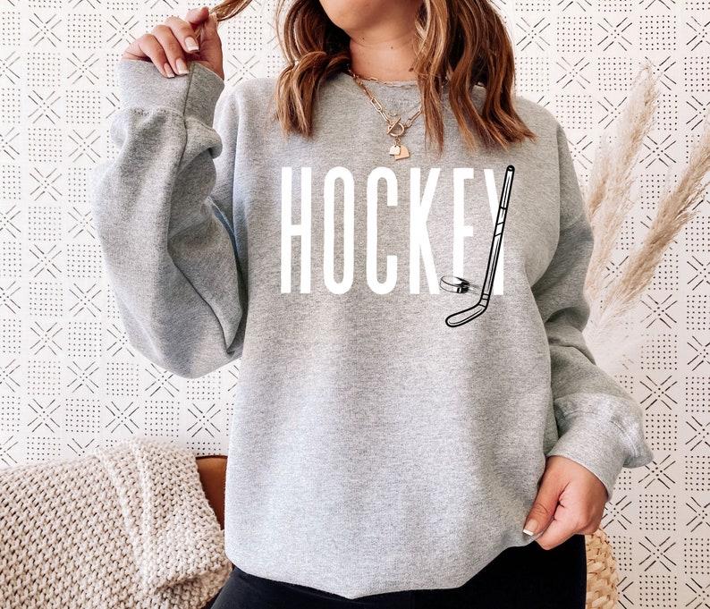 May include: Gray sweatshirt with the word "HOCKEY" printed in white and a black and white illustration of a hockey stick and puck.