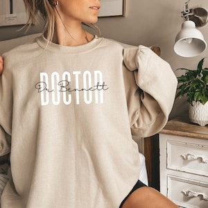 May include: A beige sweatshirt with the text "DOCTOR" in white and "Dr. Bennett" in black script.