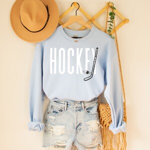 May include: Light blue sweatshirt with the word "HOCKEY" in white text and a black and white hockey stick and puck graphic.