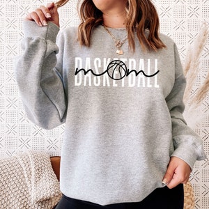 Puede incluir: Sudadera gris con el texto "Basketball Mom" en negro y blanco con un gr&aacute;fico de baloncesto.