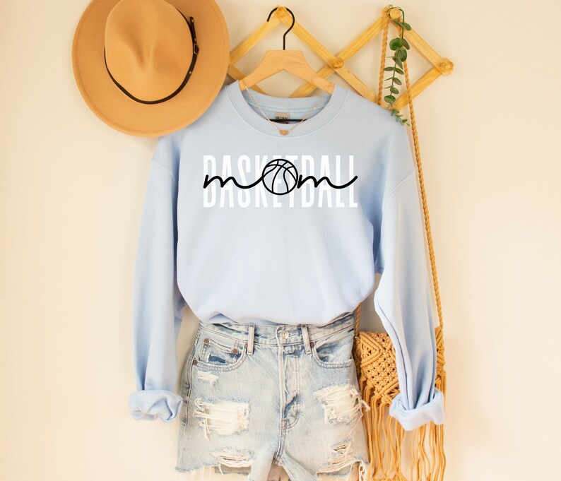 Puede incluir: Sudadera azul claro con el texto "Basketball Mom" en blanco y un gr&aacute;fico de baloncesto negro.