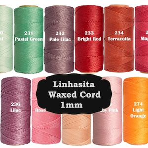 Puede incluir: Once carretes de cordón encerado Linhasita de 1 mm en varios colores, incluyendo menta, verde pastel, lila pálido, rojo brillante, terracota, magenta, lila, rosa, rosa claro y naranja claro, cada uno etiquetado con su nombre y número.
