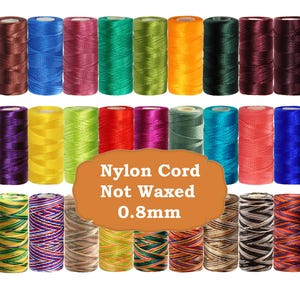 Op de afbeelding: Een verzameling kleurrijke nylon koordspoelen in verschillende tinten, waaronder rood, blauw, groen en geel. De tekst "Nylon Cord Not Waxed 0,8 mm" staat op een bruin ovaal. De spoelen zijn in nette rijen gerangschikt.