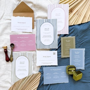 May include: A set of wedding invitations with a striped design in blue, pink, and green. The invitations include details about the wedding weekend, the finer details, and a RSVP card. The invitations are on a blue and white fabric background.