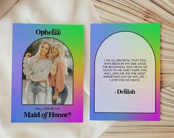 May include: A colorful card with a photo of two women in a rainbow arch. The text reads "Ophelia, Will you be my Maid of Honor?" and "I am so grateful that you have been by my side since the beginning. You mean so much to me and I hope you will join me on the most important day of my life. I love you so much. - Delilah"