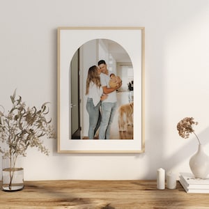 May include: A framed photograph of a family of three standing in an arched doorway. The parents are holding a baby, and a golden retriever dog is in the background.