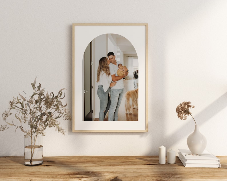 May include: A framed photograph of a family of three standing in an arched doorway. The parents are holding a baby, and a golden retriever dog is in the background.