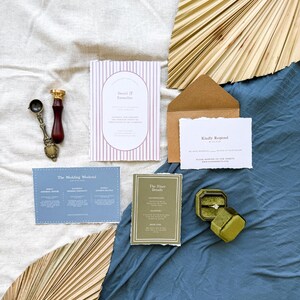 May include: Wedding invitation suite with a pink and white striped card, a blue card with the wedding weekend schedule, a green card with the finer details, a brown envelope with a white RSVP card, and a green ring box with a diamond ring.