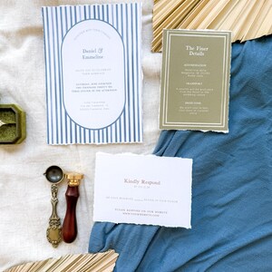 May include: A wedding invitation suite with blue and white striped paper, a brown paper card with the text "The Finer Details", and a white card with the text "Kindly Respond". The invitation suite is on a blue fabric background with a natural palm leaf fan.