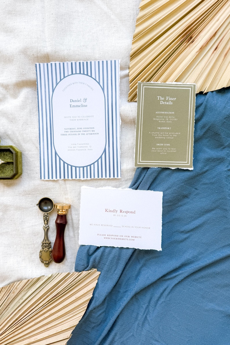 May include: A wedding invitation suite with blue and white striped paper, a brown paper card with the text "The Finer Details", and a white card with the text "Kindly Respond". The invitation suite is on a blue fabric background with a natural palm leaf fan.