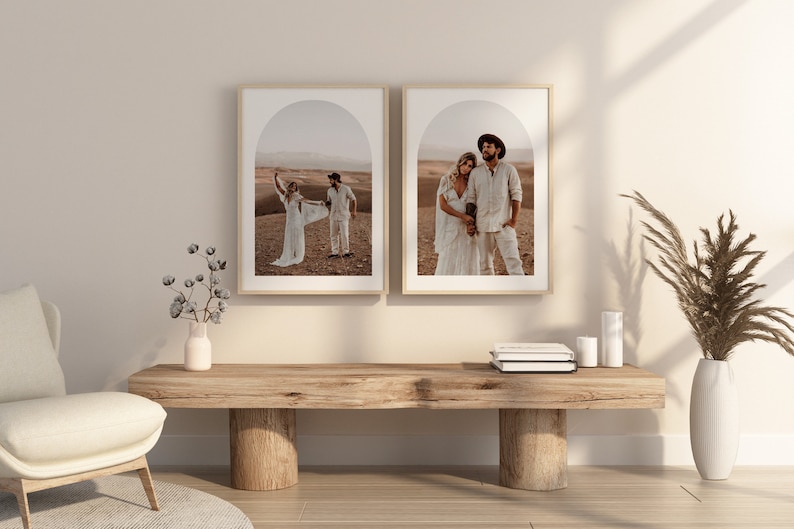 May include: Two framed photographs of a couple in a desert landscape. The photos are in a minimalist style with a white mat and a natural wood frame. The couple is wearing white clothing and is standing in a desert landscape with a large archway in the background.