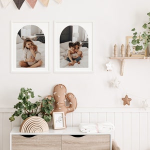 May include: Two framed photos of children in a nursery setting. The photos are in white frames with an arched opening. The photos are hung on a white wall with a white wainscoting paneling. The photos show children hugging and smiling.