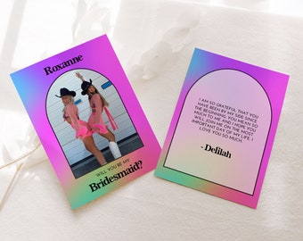 May include: A pink and blue gradient card with a photo of two women in cowboy hats and pink outfits. The text on the card reads "Roxanne, Will you be my Bridesmaid?" and "I am so grateful that you have been by my side since the beginning. You mean so much to me and I hope you will join me on the most important day of my life. I love you so much - Delilah"
