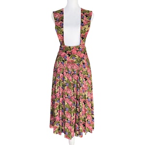 May include: A vintage floral print dress with suspender straps. The dress features a black background with pink, purple, and green floral patterns. The skirt is pleated and falls to mid-calf length, creating a classic silhouette.