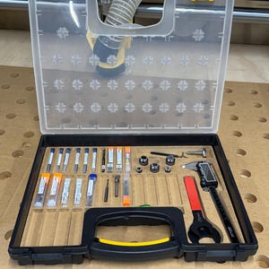May include: A black plastic case with a yellow handle, containing a variety of tools, including drill bits, a wrench, a caliper, and other small tools. The case is open and the tools are visible.