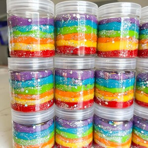 May include: Clear plastic jars filled with colorful, layered rainbow-colored playdough. Each jar has a clear lid and is sprinkled with silver glitter. The playdough layers include red, orange, yellow, green, blue, and purple.