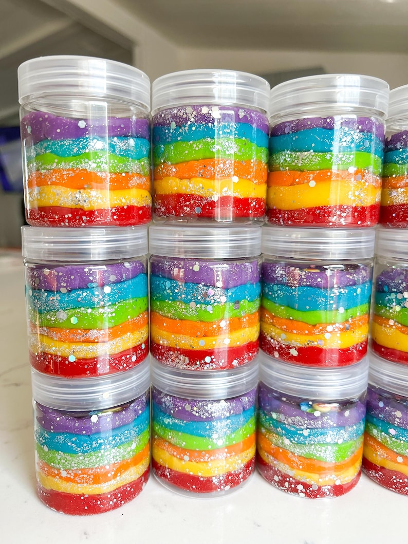 May include: Clear plastic jars filled with colorful, layered rainbow-colored playdough. Each jar has a clear lid and is sprinkled with silver glitter. The playdough layers include red, orange, yellow, green, blue, and purple.