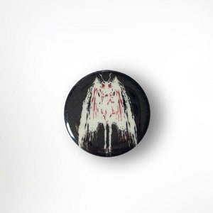 May include: A black button with a white and red moth design. The moth has a large wingspan and is in a spread-wing pose.