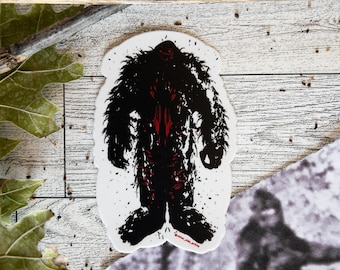 May include: Black and red silhouette sticker of a Bigfoot or Sasquatch. The sticker is on a white background with a white woodgrain surface behind it.