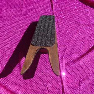 May include: A wooden boot jack with a gray felt pad on top. The boot jack is brown and has a simple design.