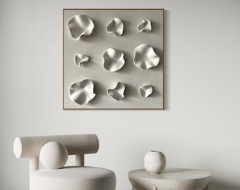 Può includere: Una sedia rotonda bianca con uno schienale cilindrico e una seduta rotonda. La sedia è di fronte a un muro bianco con un'opera d'arte incorniciata che presenta un design bianco astratto. Un piccolo tavolino rotondo bianco con una superficie testurizzata è in primo piano.