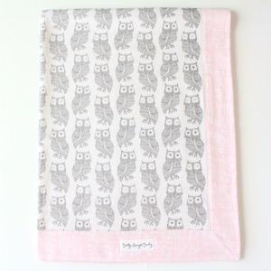 May include: A white baby blanket with a pink border and a gray owl pattern. The blanket has a tag that says "Belly Lounge Baby".