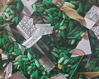 May include: Green and gold glitter rice with torn pieces of US dollar bills. The bills are scattered throughout the rice.