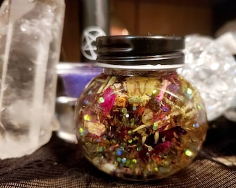 May include: A clear glass jar filled with dried flowers, herbs, and glitter. The jar has a black lid.