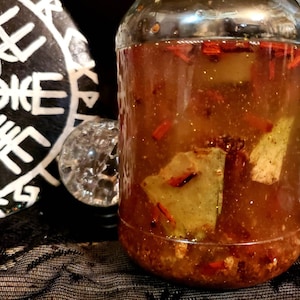 May include: A clear glass jar filled with a brown liquid and red and green pieces. The jar is sitting on a black lace surface.