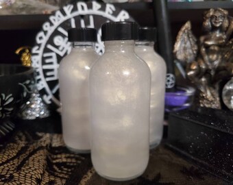 May include: Three clear glass bottles with silver glitter inside. The bottles have black lids and are sitting on a black surface.