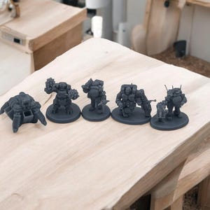 May include: Five gray 3D printed miniature figures on black bases. The figures are robots or mechs with various weapons and details.