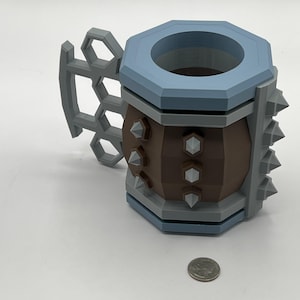 May include: A brown and light blue mug with a gray hexagonal handle and gray spikes on the side. The mug features a brown cylindrical body with gray hexagonal accents and a light blue rim. A US quarter is placed next to the mug for scale reference.