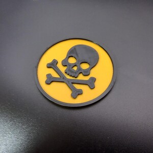 May include: A round sticker with a skull and crossbones design, in black and yellow.