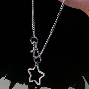 May include: A silver chain necklace with a star-shaped charm and a silver clasp. The chain is a curb chain style.