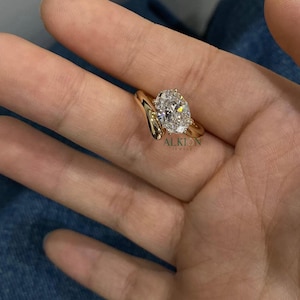 May include: A gold engagement ring with a large oval-shaped diamond. The ring has a unique, curved band.