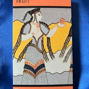 May include: A tarot card with the word "FRUIT" at the top and a woman holding a red fruit in her hand. The card is orange and has the words "Delight - Discover - Serendipity" at the bottom.