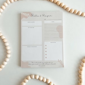 May include: A beige Bible and Prayer notepad with sections for book and chapter, key scripture, and notes. The notepad includes the text "You will seek me and find me when you seek me with all your heart." Decorative wooden beads surround the notepad.
