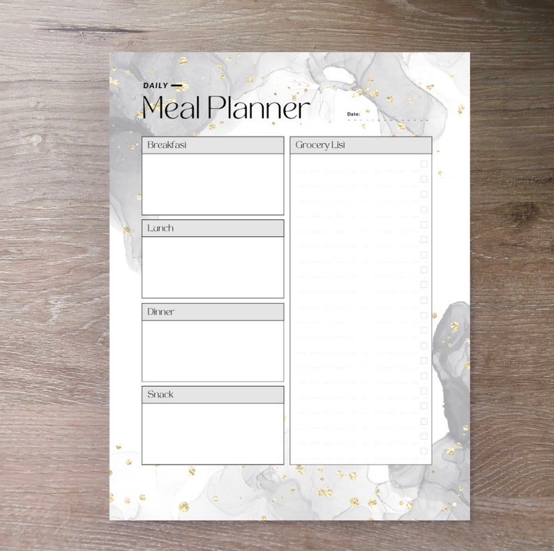 May include: A white meal planner with a gray and gold marble design. The planner has sections for breakfast, lunch, dinner, and snack. It also includes a grocery list with checkboxes.