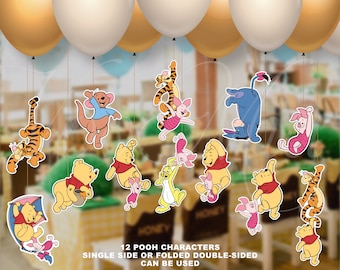 May include: Twelve Winnie the Pooh character cutouts, including Tigger, Piglet, Eeyore, and Kanga, hanging from gold and white balloons. The cutouts are printed on white cardstock and can be used single-sided or double-sided. "12 POOH CHARACTERS SINGLE SIDE OR FOLDED DOUBLE-SIDED CAN BE USED" is printed at the bottom of the image.