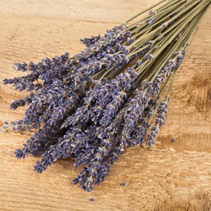 May include: A bunch of dried lavender flowers with purple blooms and green stems. The lavender is arranged in a bouquet and is lying on a wooden surface.