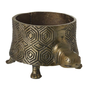 May include: A bronze-coloured turtle-shaped planter. The planter features a textured geometric pattern on its shell and a turtle head and legs. It is designed to hold small plants or decorative items. The overall design is detailed and artistic.