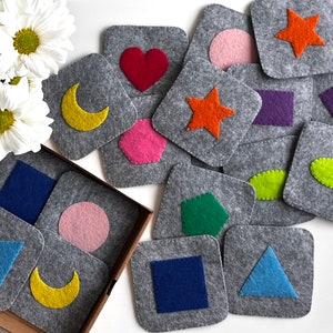 Könnte beinhalten: Ein Set aus Filz-Spielsteinen mit verschiedenen Formen und Farben. Die Formen umfassen einen Stern, einen Halbmond, ein Herz, einen Kreis, ein Sechseck, ein Quadrat, ein Fünfeck, ein Dreieck und ein Rechteck. Die Farben umfassen Rot, Orange, Gelb, Grün, Blau, Lila und Rosa.