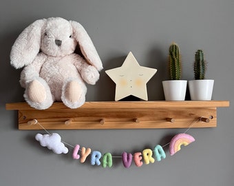 May include: A wooden shelf with a white bunny plush toy, a star-shaped nightlight, two potted cacti, and a rainbow-coloured felt banner that reads "LYRA VERA".