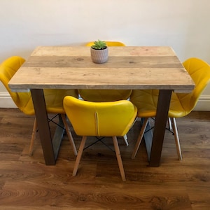 May include: A dining table with a light brown wooden top and dark metal legs, surrounded by four yellow chairs. A small potted succulent sits on the table. The chairs have wooden legs and a quilted back design.